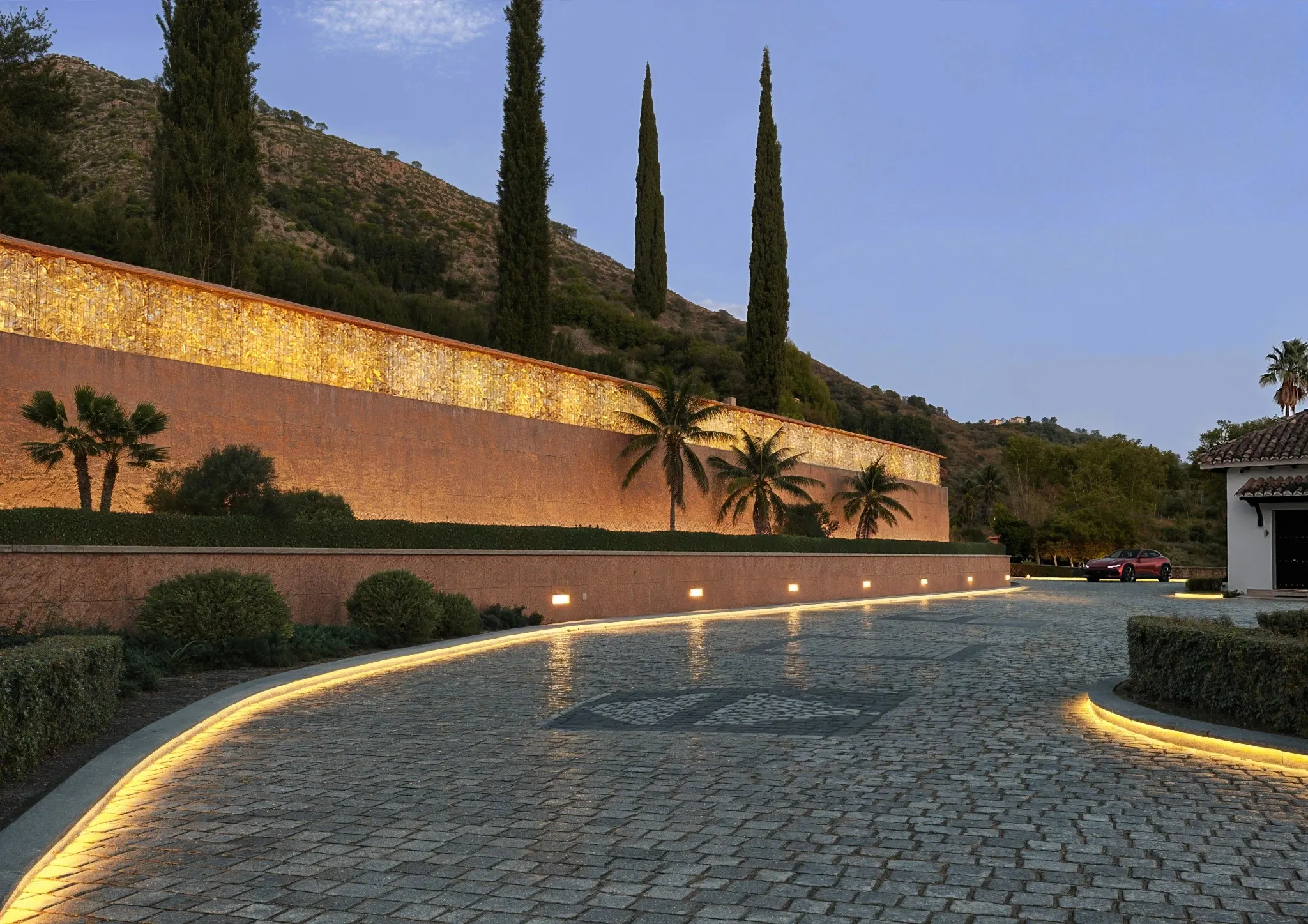 Curved cobbled driveway with illuminated gabion wall, palms and cypress trees in Istán.