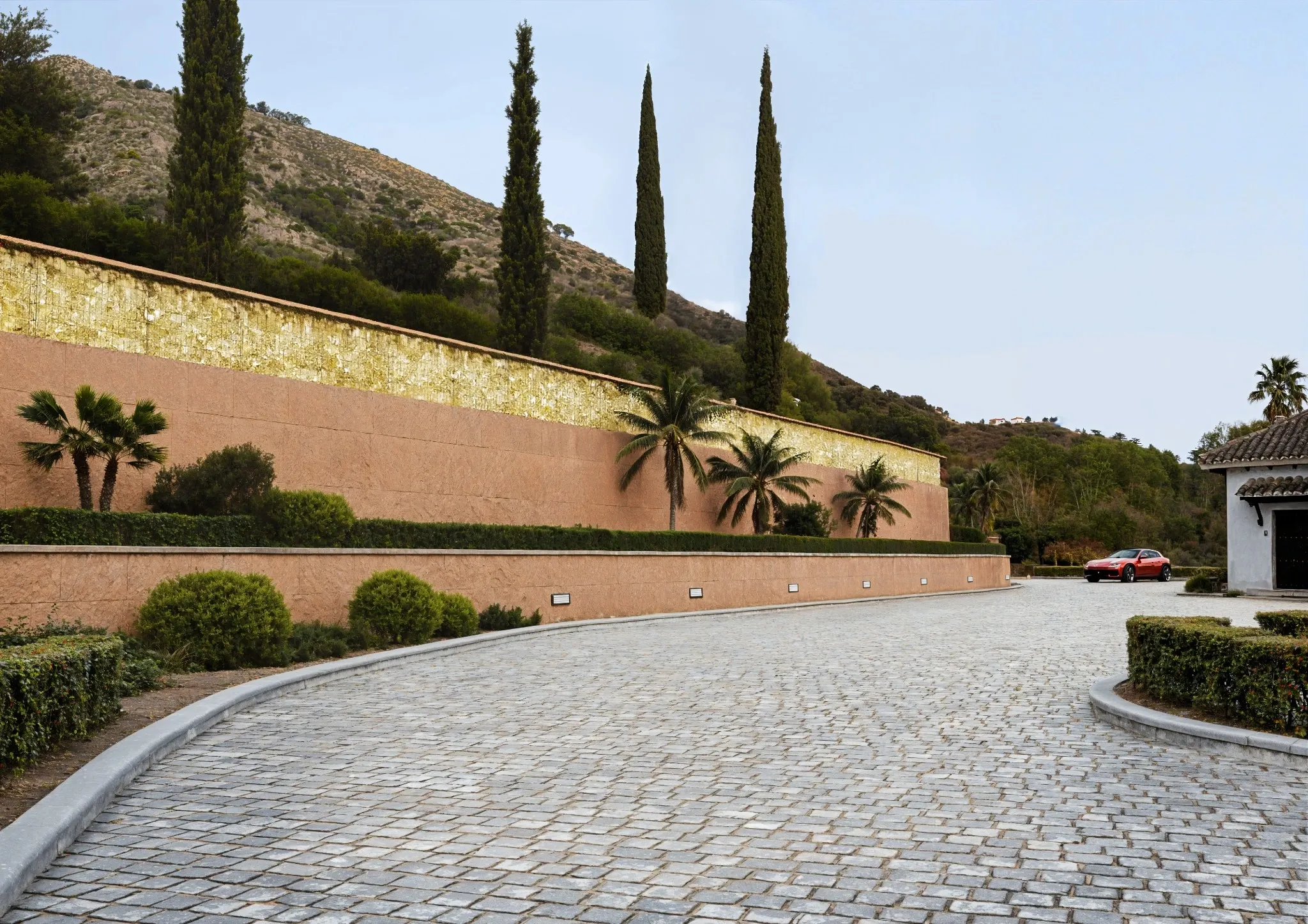 Daylight view of the entrance driveway, terraced planting and warm-toned walls against the hillside.