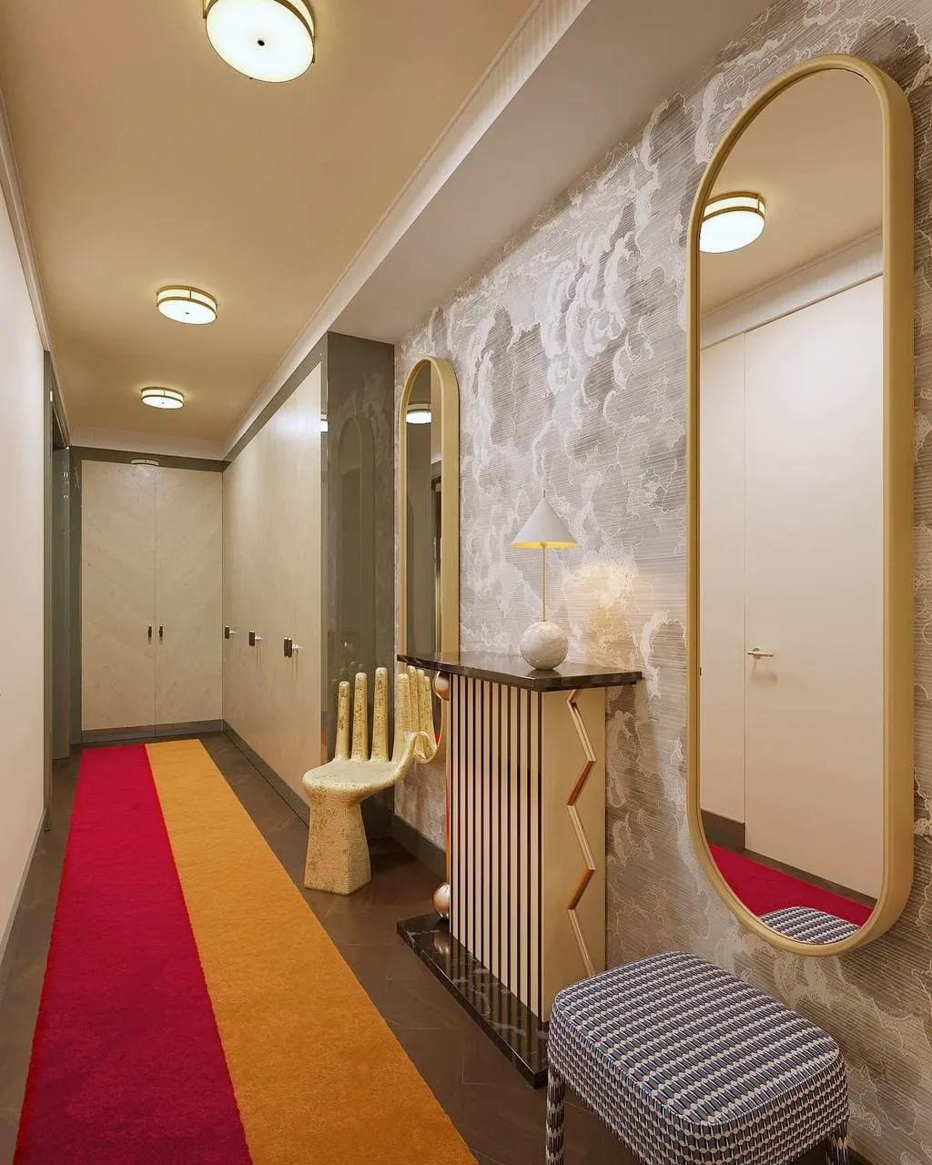 Hallway with tall mirrors, a sculptural hand chair and a red and ochre runner